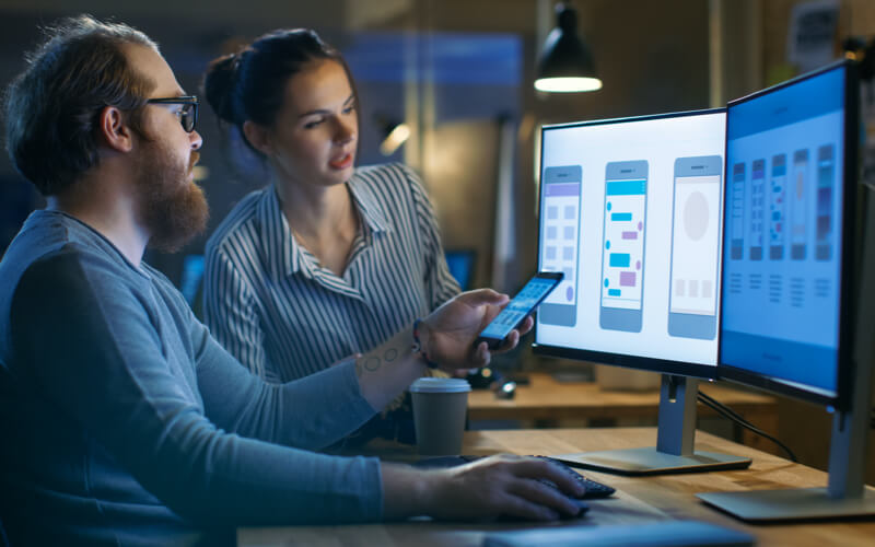 a dimmed light, a man holding a phone, and a woman next to him looking at the screen. 
